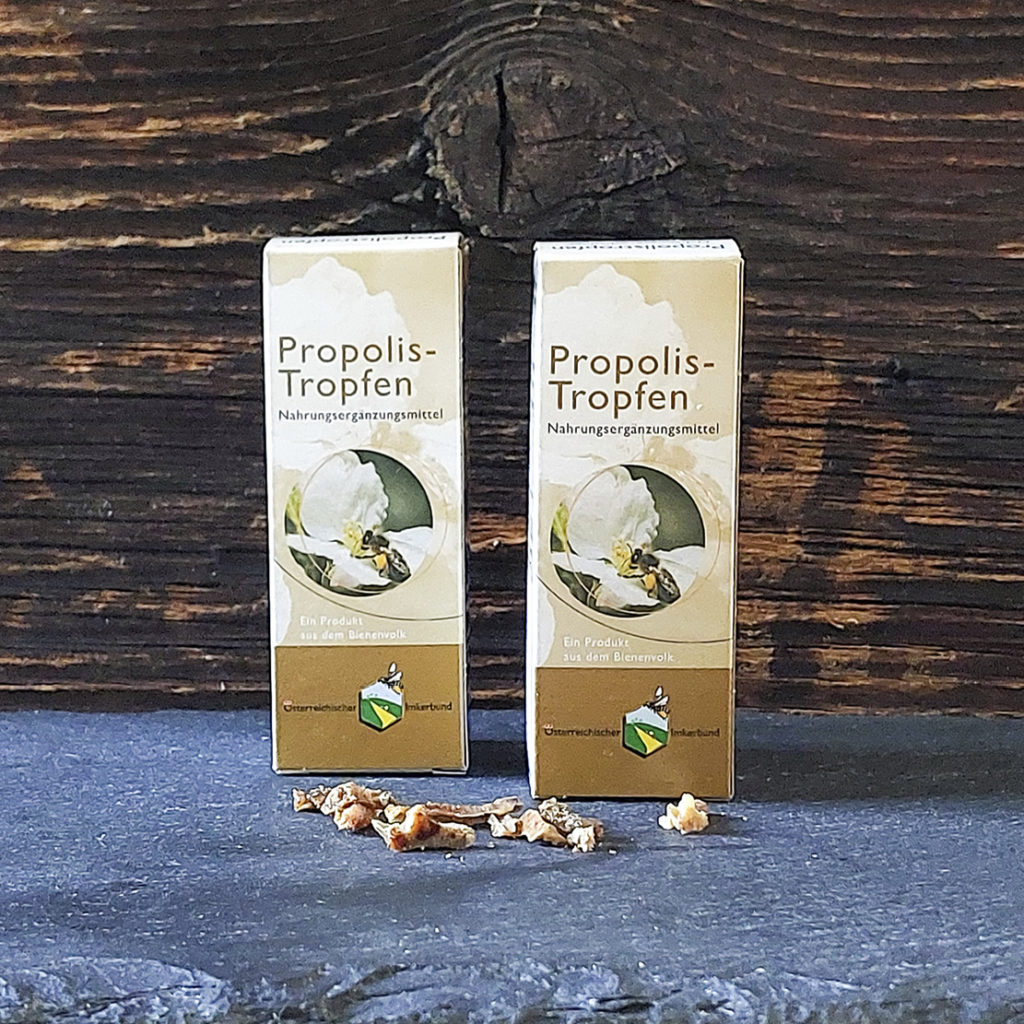 2 Schachteln Propolistropfen auf Schiefertafel mit Propolis im Vordergrund