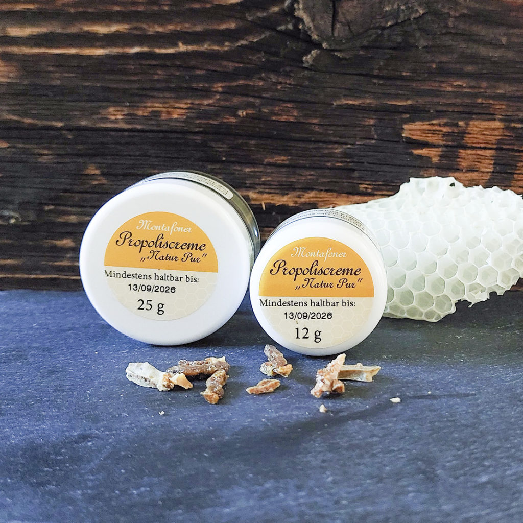 zwei Dosen Propoliscrme mit Propolis im Vordergrund und Waben im Hintergrund