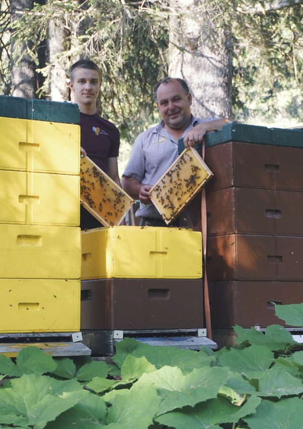 Imker Simon und Andreas zwischen Bienenstöcken mit Honigrahmen in den Händen