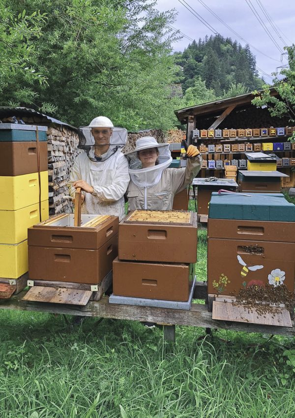 Simon mit Helferin in Imkeranzug zwischen Bienenstöcken